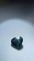 Close-up photo of the heart-shaped multicolored sapphire gemstone highlighting its blue, green and yellow hues and faceted cut.
