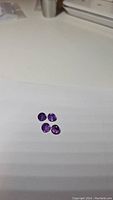 Four round cut calibrated amethyst gemstones displayed on white background, showing size and color.