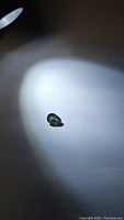 Photo shows pear shaped green sapphire with visible facets under light, color shows green with blue undertones.