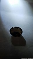 Photo of oval cut natural smokey quartz gemstone showing faceted surface and dark translucent brown color.