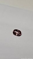 Close-up photo of an oval cut natural pink champagne zircon gemstone showing its pinkish-brown color and facets.