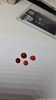 Four small polished Carnelian cabochon gemstones in red and orange shades shown on white background with a partially visible card.