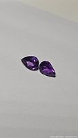 Pair of deep purple pear cut amethyst gemstones shown on white background.