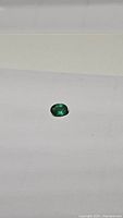 Close-up of oval natural emerald gemstone on white background showing vibrant green color and luster.