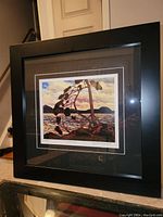 Framed fine art print in black frame with double matting showing a landscape with a bent pine tree by water and hills.