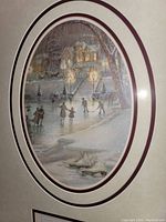 Close-up image of the oval vignette showing people ice skating in a winter nighttime scene with a house and trees in the background and a pair of skates in foreground.