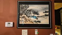 Framed Asian landscape painting hanging on a brown wall, visible alongside thermostat and light switches.