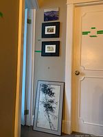 Four framed art pieces: one large Japanese watercolor painting leaning against wall showing bamboo and inscriptions, two smaller framed signed watercolours on the wall, and one framed photograph on board above.