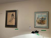 Two framed art pieces hanging on a wall: Left is a charcoal nude drawing, right is a watercolor painting of The Western Wall.