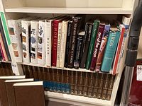 Wide view of shelf showing mixed collection of hardcover art, history, and reference books including Encyclopedia Britannica 1988 set below.