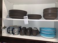 Cupboard shelf with Noritake stoneware plates, bowls, grey mugs, Mexican patterned mugs, and blue Euro Samica bowls