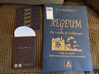 Photo of the decorative board cover with gold embossed title 'Aegeum the cradle of Hellenism' and a set of six postcards