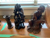 Photo featuring all three wood carvings on a wooden surface near window light. Includes two African figurines and one Chinese figurine.