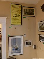 Four framed wall prints hung on a tan wall including a large yellow Italian announcement poster and three other framed prints of architecture or landscapes.