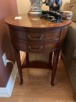 Front view of round hardwood side table showing leather top with gold tooling and two drawers with brass handles.