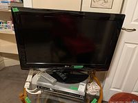 Front view of LG 32 inch TV placed on a wooden chair with Toshiba DVD/VHS combo below it, remotes and cords on top