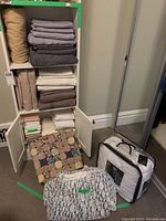 Full view of assorted linens on shelves including folded sheets, pillowcases, blankets, and a packaged mattress protector on floor leaning against shelf.