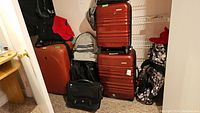 Large orange Heys hard shell suitcase with four wheels standing upright with other luggage and bags.