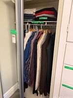 Full closet view showing hanging suits, dress shirts, and folded sweaters on top shelf