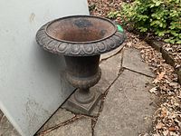 Full side and front angled views of the single large metal urn placed on an outdoor stone patio, showing rust and wear.