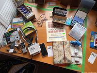 Wide view showing assorted office accessories on a desk including electronics like an iPhone and battery charger, eyeglasses, Rolodex, and media discs.