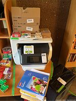 HP OfficeJet Pro 8740 printer front view with assorted cartridges and paper on top and nearby surfaces