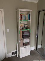 Front view of the shelving unit displaying books on the top two shelves, folded linens on the next two shelves, and closed cabinet at the base.