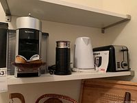 Nespresso coffee maker, milk frother, electric kettle, and Cuisinart toaster on a shelf.