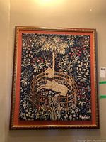 Full view of the framed tapestry depicting a white unicorn inside a wooden fence surrounded by floral patterns on a blue background.