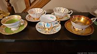 Set of five vintage teacups with matching saucers on dark wood surface, showcasing varied color and gold decorative detailing