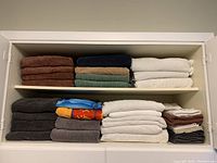 Photo showing stacked bath towels and hand towels of varied colors and sizes on white shelving.