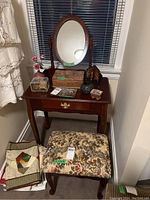 Full view of vanity table with attached oval mirror, one drawer, and matching tapestry bench in front. Items and some objects on the table shown.