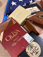 Photo of open wooden cigar boxes with visible branding including Oliva Serie V Liga Especial and HC El Corojo, along with other natural wood boxes