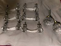 Full set of six clear glass drawer pulls and two clear faceted knobs displayed on white fabric background, showing attached screws and wing nuts for installation.