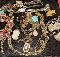 Overview of assorted costume necklaces including carved white jade, amethyst, rose quartz, and other stone pendants with various gold-tone and beaded chains.