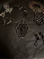 Photo showing the black jeweled necklace medallion with ornate design, paired with 3 sets of black earrings and an ornate pin with large stone.