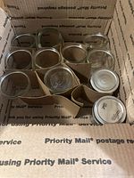 Box containing 12 Ball glass jelly jars arranged with cardboard dividers, some jars have lids and some are missing lids.