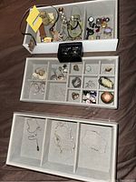 Photo showing multiple compartments containing costume jewelry including earrings, rings, pendants, and cufflinks with New York Yankees emblem.