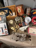 Photo shows a collection of vintage advertising tins, a mini tool kit in packaging, decorative and kitchen items on a table.