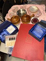 Full view of the items including brown glazed soup crocks with lids, clear glass oyster dishes arranged on a tray, stainless steel incense bowl, leather coasters in a box, and 'The Travel Book'