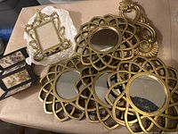 Collection of gold-toned decorative items including round mirrors, small frame, and decorative boxes on a table.