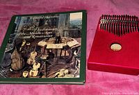 Red klimba instrument next to a book on musical instruments of the Middle Ages and Renaissance.