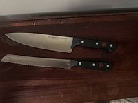 Wusthof Gourmet black handled knives - chef and serrated blade shown on wooden surface
