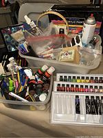 Full overview of all art supplies in plastic bins and bags showing assortment of paints, pens, pencils, crayons, brushes, spray paint and craft tools.