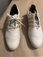 Top view of pair of white Adidas cleats showing leather upper and laces.