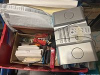 Wide shot of box with envelopes, staples, cards, paper, folders, and iHome player with remote and speakers