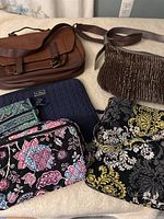 Brown Aldo leather messenger bag, glittery brown purse, several Vera Bradley fabric purses in floral and patterned designs on a light background