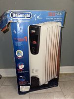 Photo of the DeLonghi Safe Heat electric oil-filled radiator heater in its original blue box with branding and product details visible.