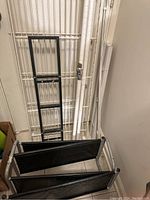 Black metal shelving frame parts with mesh panels and aluminum window shade sections laid against wall