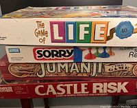 Stack of four vintage board games: The Game of Life, Sorry, Jumanji, Castle Risk showing box spines with logos and art.